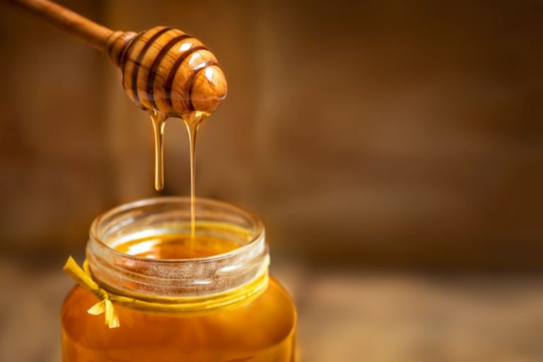 A jar of liquid honey with a honey wand dripping honey back into jar