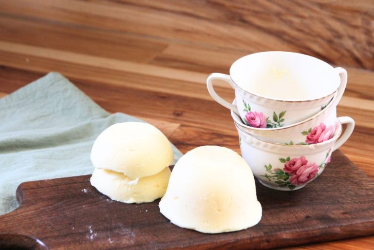 Homemade butter sitting on a wooden cutting board, fresh from teacup molds