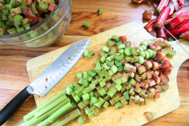 red and green rhubarb stalks on a cutting board, being sliced into 1/2 inch pieces