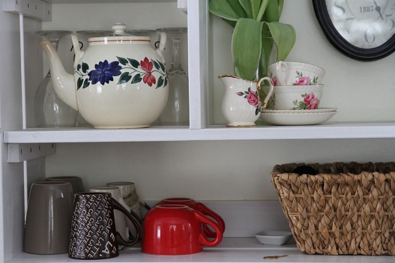 Open shelving in kitchen displaying tea cups, tea pot and a basket