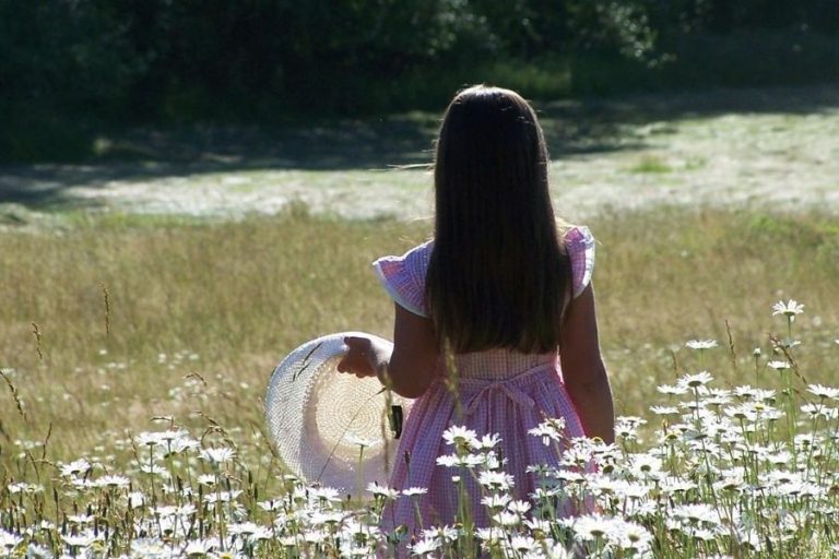 A little girl holding a sunhat in hayfield