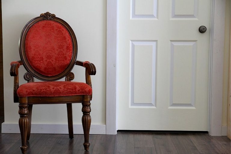 A red armchair next a cream and white, painted door