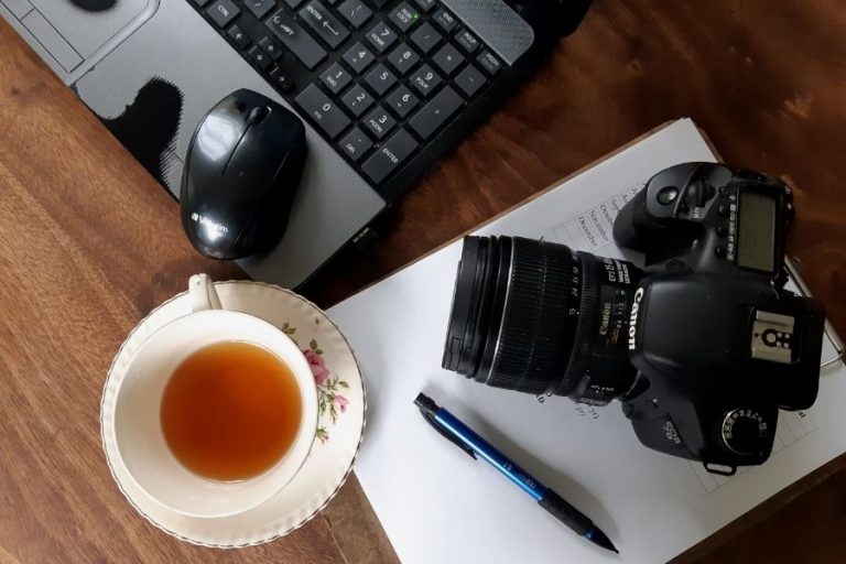 A blogger's workspace on a the kitchen table with computer, camera and a cup of tea