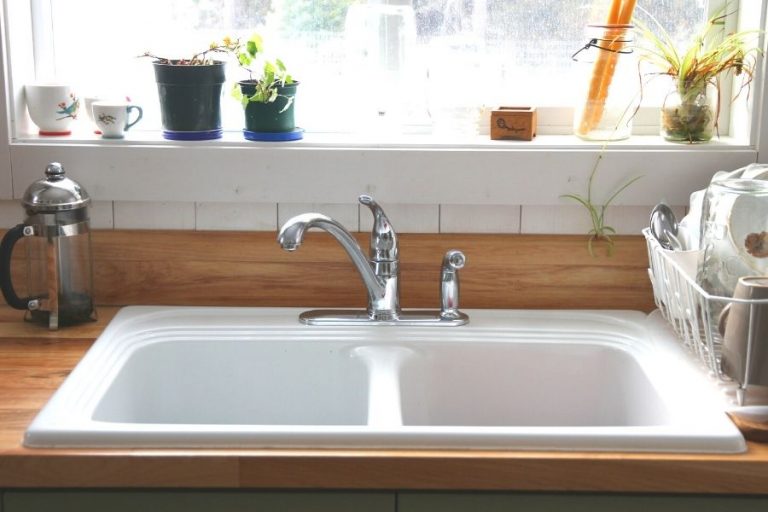 A white kitchen sink with a stack of clean dishes in the drying rack