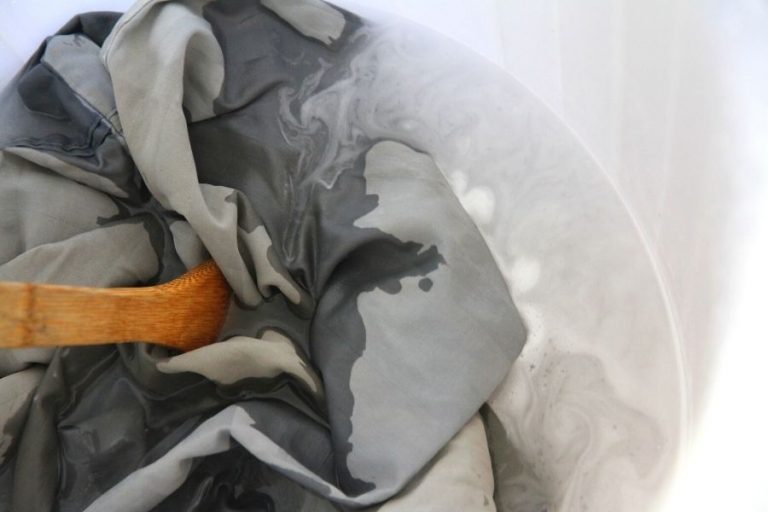 A blue bedsheets being submerged in a pail of hot water, show you how ot strip your laundry of build up