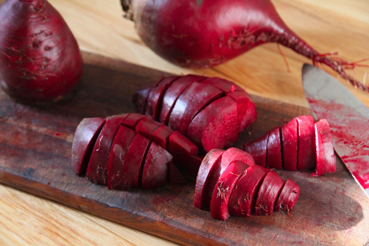 Red beetroot being sliced into 1/2 inch thick chunks on a walnut wood cutting board. 