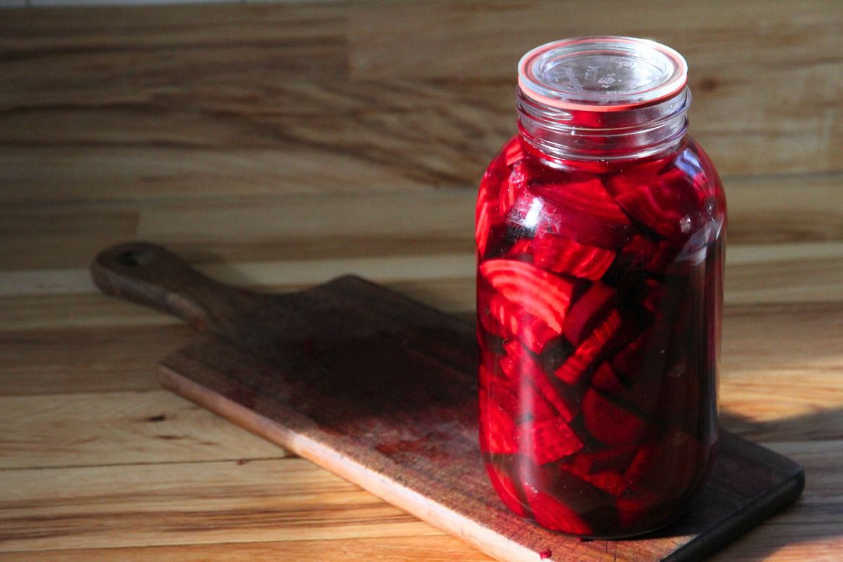A large glass jar with a lid, filled with beets, water and salt.