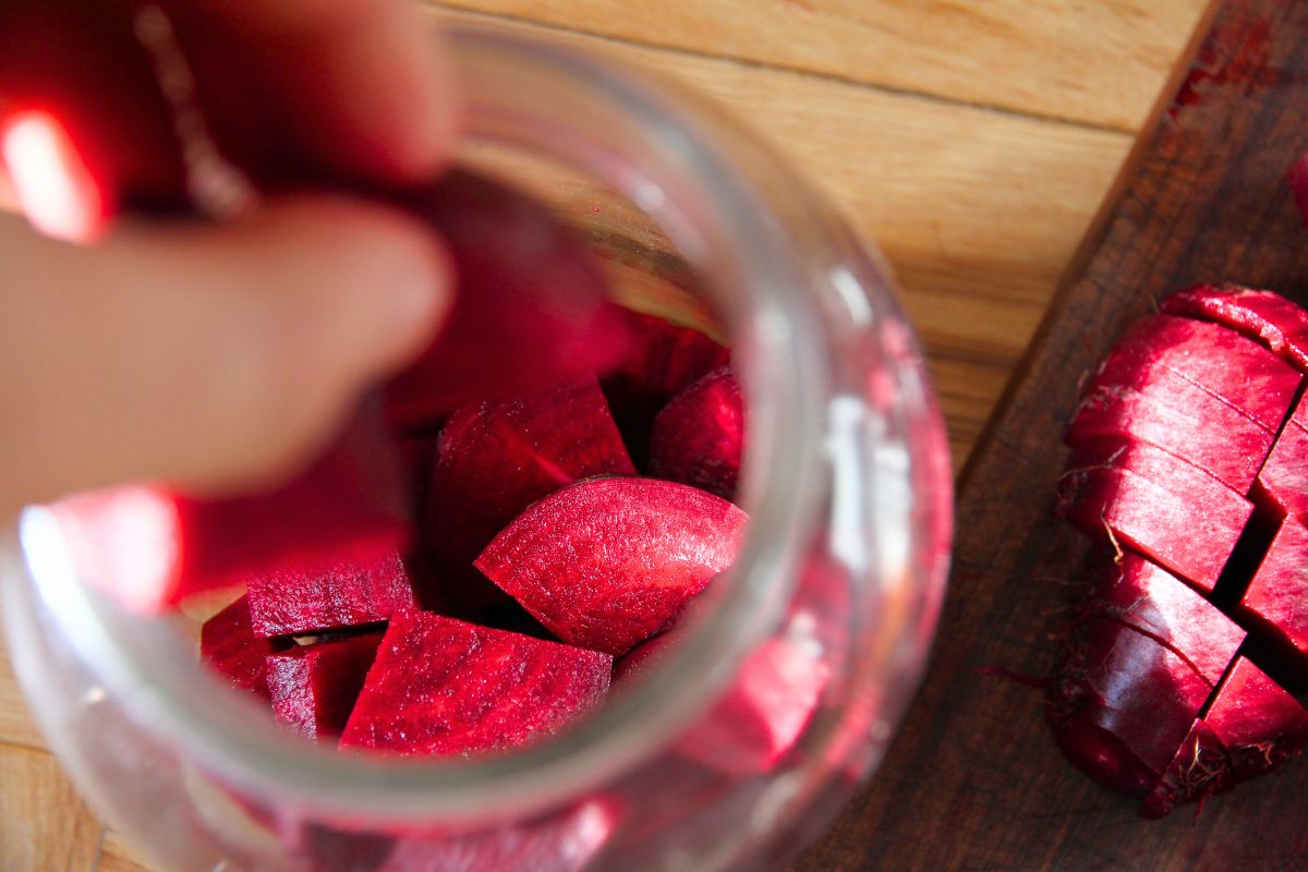 Stuffing a large glass jar with chunks of sliced red beets. 