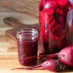 A jar of fermenting beet kvass, raw beets and a mason jar filled with fully fermented beet kvass.