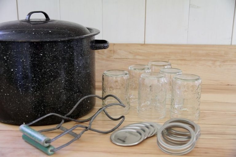 an black enamel canner, a jar lifter, canning jars, rings and bands sitting on a wooden countertop