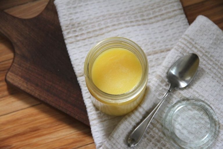 a jar of melted chicken fat sitting on a wooden cutting board with a stainless steel spoon and glass lid sitting off to the side