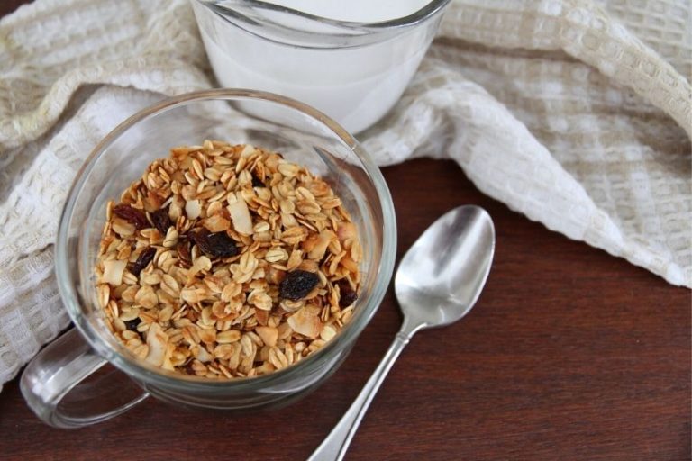 a clear glass bowl of granola with a silver spoon on the right side, ready for an addition of milk or yogurt