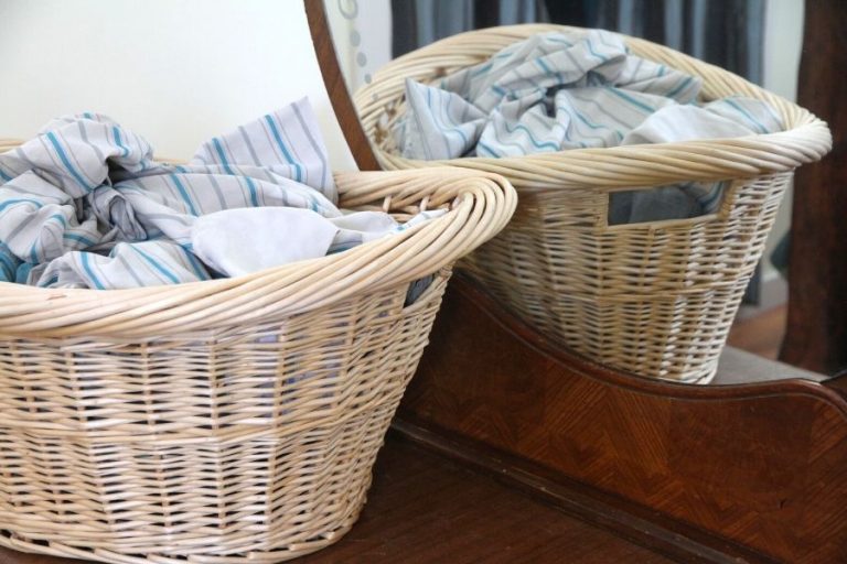 a basket of white and blue striped sheets sitting on a dresser top with a mirror casting a reflection