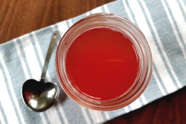 a jar of bright red strawberry vinegar sitting on a blue and white tea towel