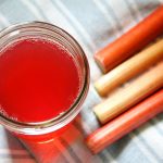 a jar of rhubarb juice concentrate on a blue cloth with red rhubarb stalks nearby
