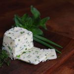 a square of herb butter surrounded by fresh herbs on a wooden cutting board