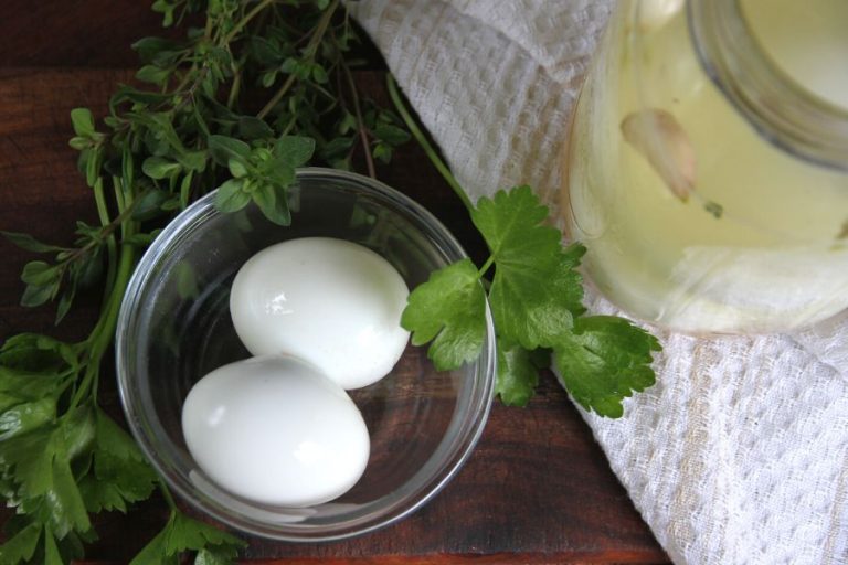 Two fermented hard boiled eggs sitting in a clear glass bowl next to a jar of fermenting hard boiled eggs