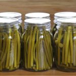 a row of 7 pint jars filled with pickled garlic scape stems