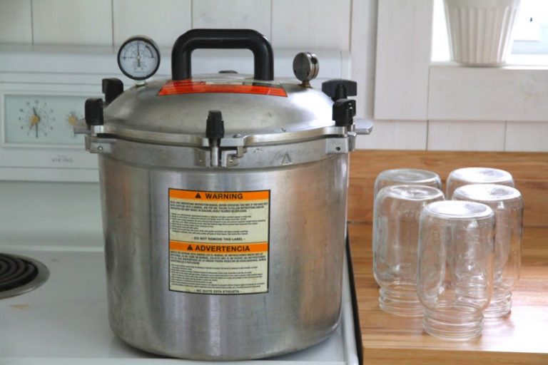 A pressure canning sitting on a white stove top with a stack of jars on the counter to the right
