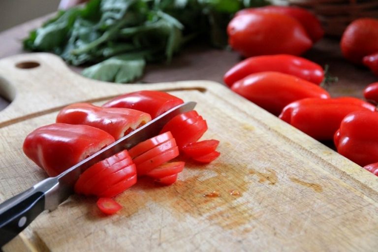 ripe red paste tomatoes being sliced into rings on a wooden cutting board