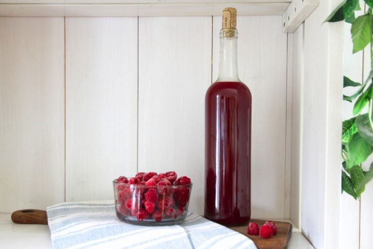 A clear bottle with a cork filled with red raspberry vinegar.