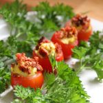 a row of stuffed cherry tomatoes on a white plate, garnished with sprigs of green parsley