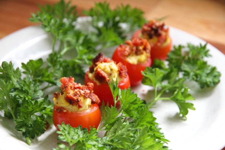 a row of stuffed cherry tomatoes on a white plate, garnished with sprigs of green parsley