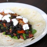 an open tortilla on a white plate revealing home canned black bean filling