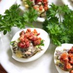 stuffed deviled eggs sitting on a white platter with parsley on the side
