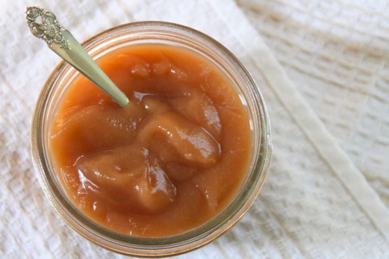 a jar of finished oven apple butter with a silver spoon