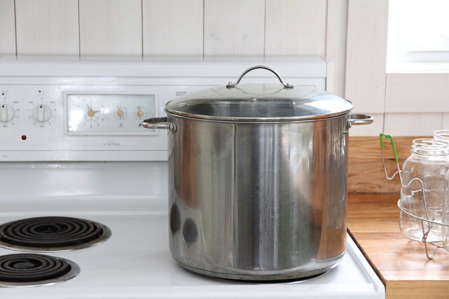 A large, stainless steel water bath canner on a white kitchen stovetop.