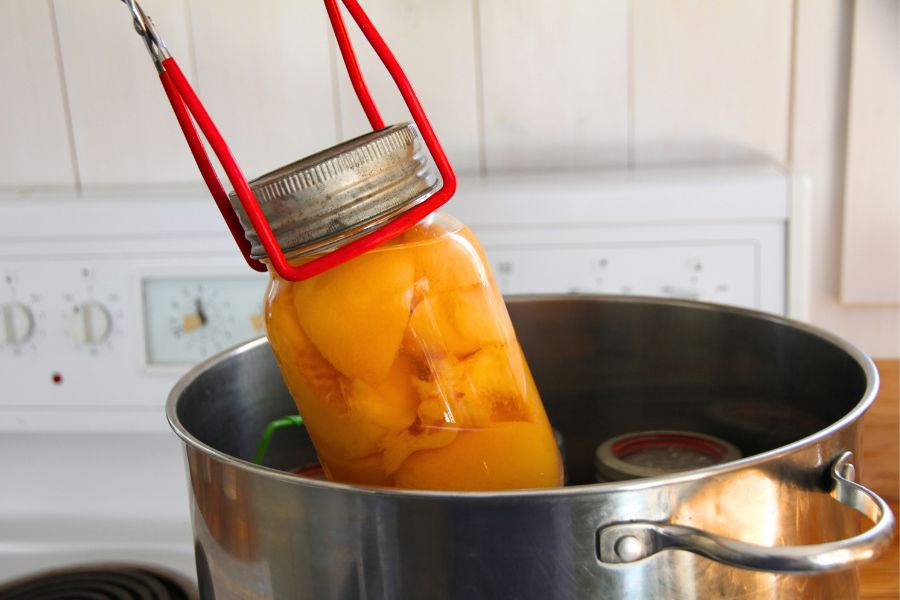 A jar of peaches being lifted from a boiling water bath canner.