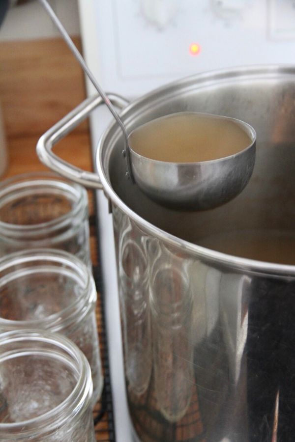Hot venison stock being ladled into glass jars for canning.