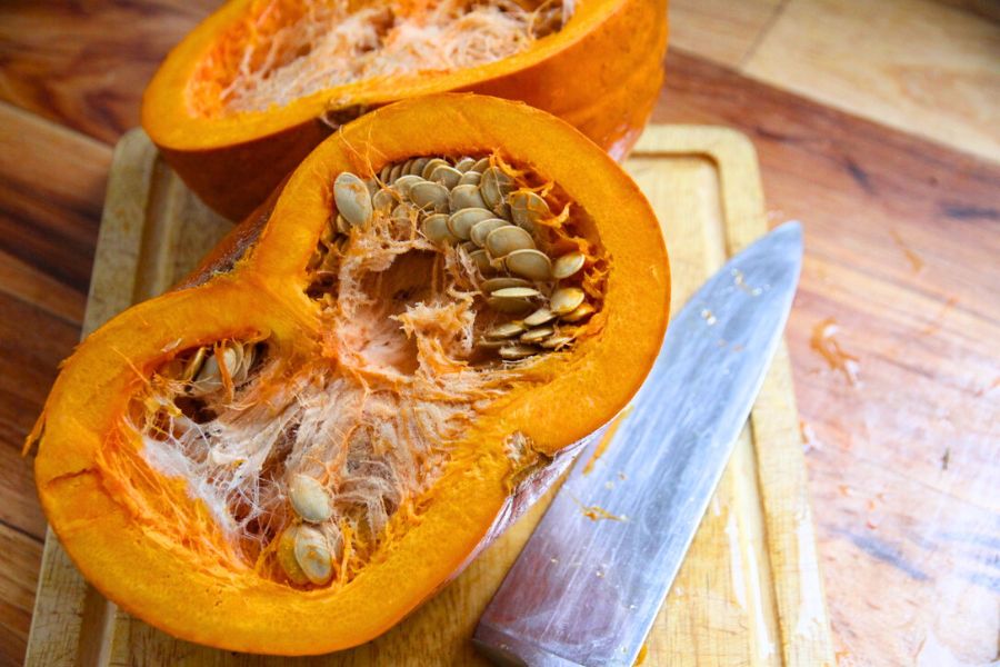 A fresh pumpkin cut in half on a cutting board, ready to have seeds removed.