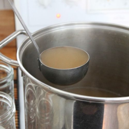 Hot venison stock being ladled into glass jars for refrigeration.