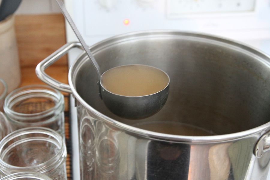 Hot venison stock being ladled into glass jars for refrigeration. 