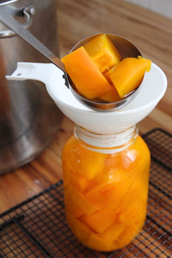 Ladling hot pumpkin and boiling water into a quart jar.