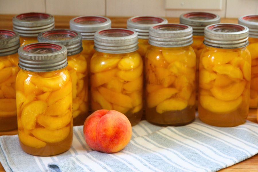 Quart-size jars of home canned peaches cooling on the kitchen counter.