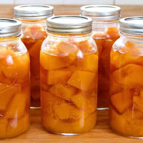 Jars of home-canned pumpkin sitting on a wooden kitchen counter.