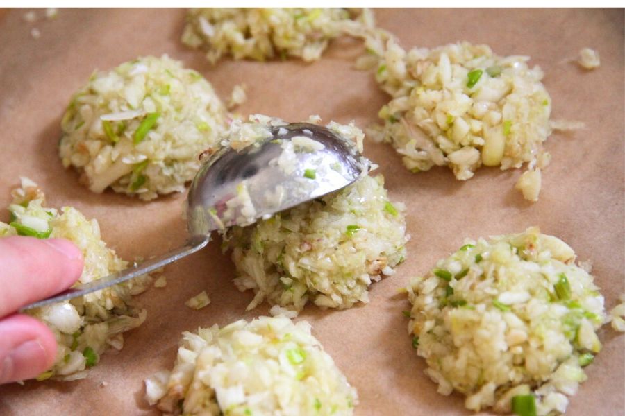 Tapping a filled tablespoon of minced garlic out onto parchment lined baking pan.