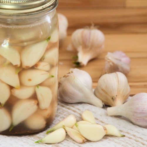 Fermented garlic in a glass jar surrounded by whole and peeled garlic cloves.