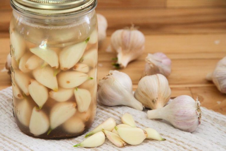 Fermented garlic in a glass jar surrounded by whole and peeled garlic cloves.