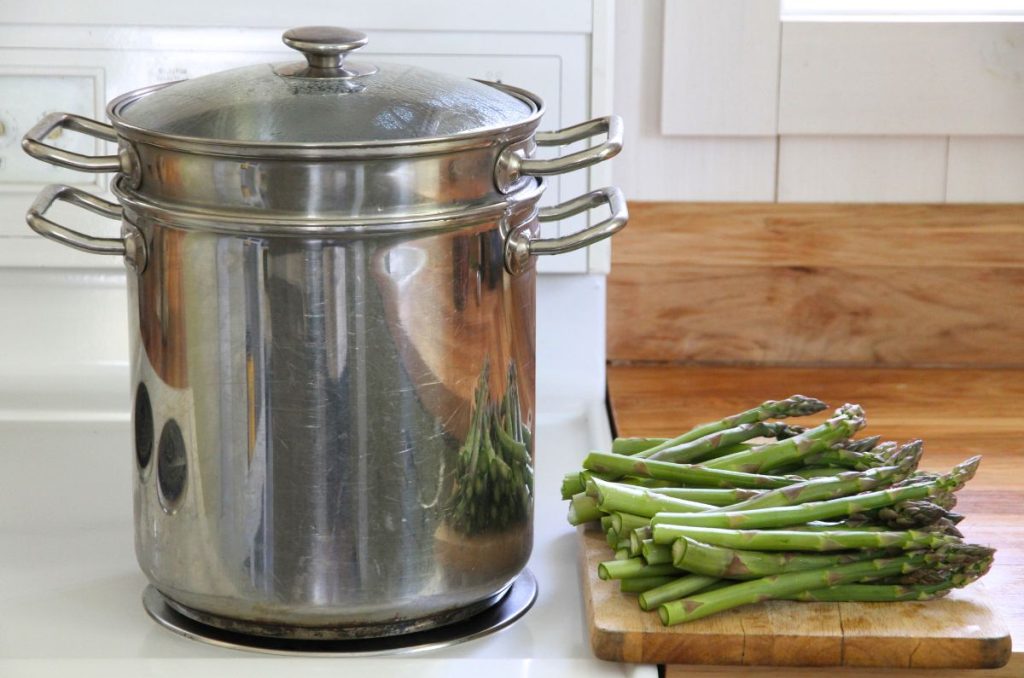 A large pot of water heating on the stove, with prepared asparagus waiting by the side.