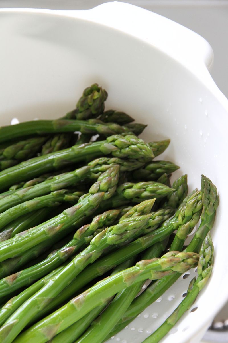Blanched green asparagus draining in a large white colander.