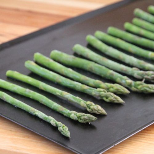 Frozen asparagus spears in a single layer on a baking sheet.