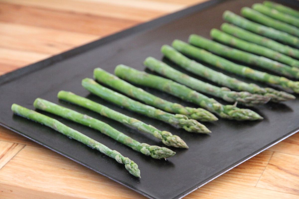 Frozen asparagus spears in a single layer on a baking sheet.
