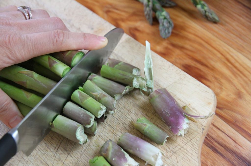 Trimming the tough ends of asparagus spears on a cutting board.