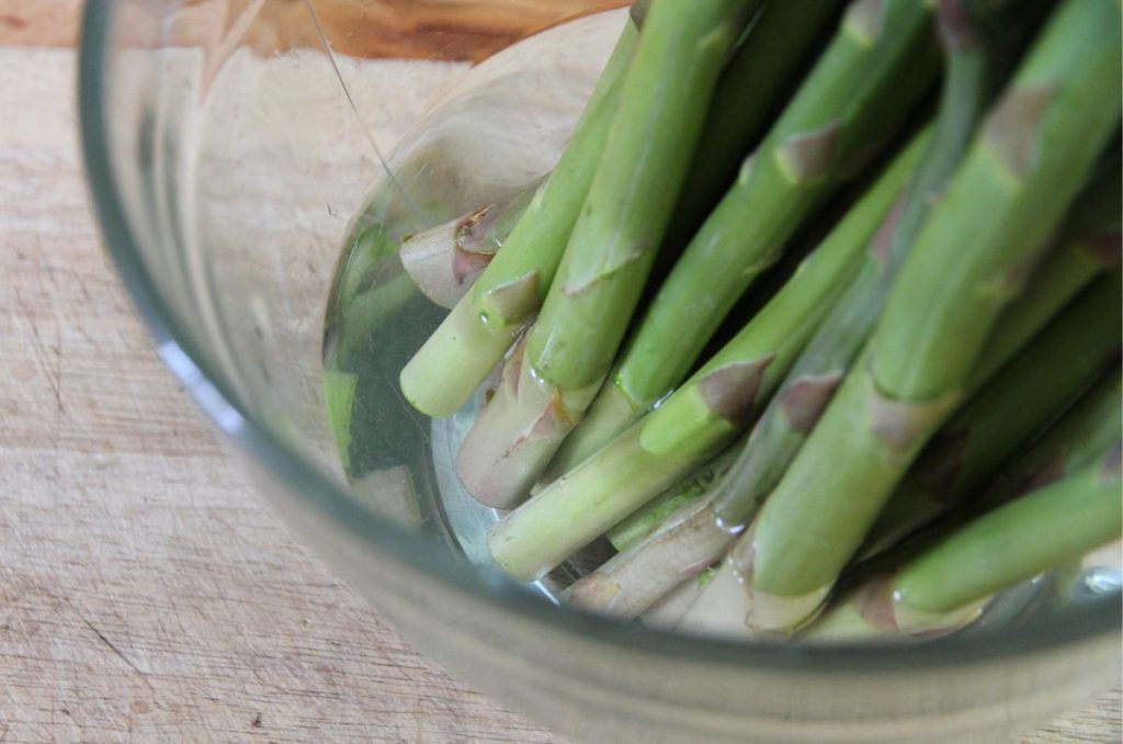 Freshly trimmed asparagus sitting upright in a deep bowl of water.