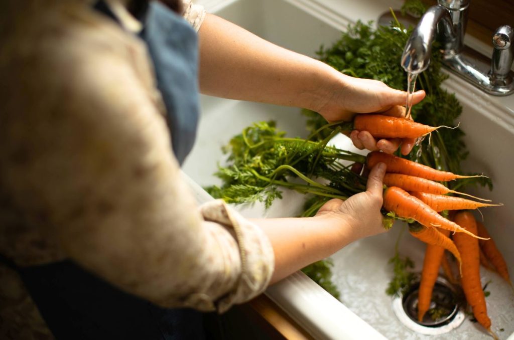 Washing fresh carrots at a white kitchen sink.