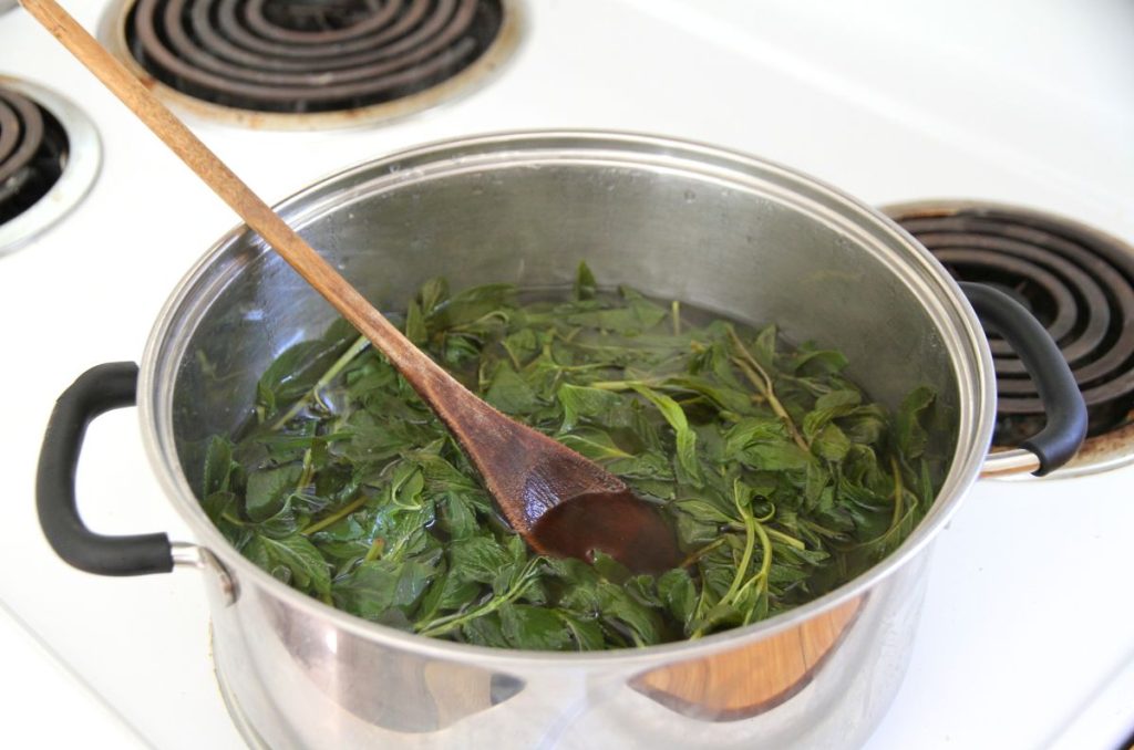 Mint being stirred down into the water with a wooden spoon.